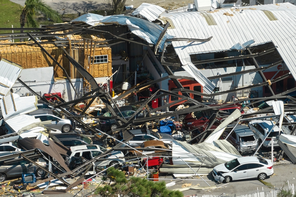 The aftermath of a large storm is shown, a warehouse ceiling is destroyed and metal is draped over where the roof used to be. 