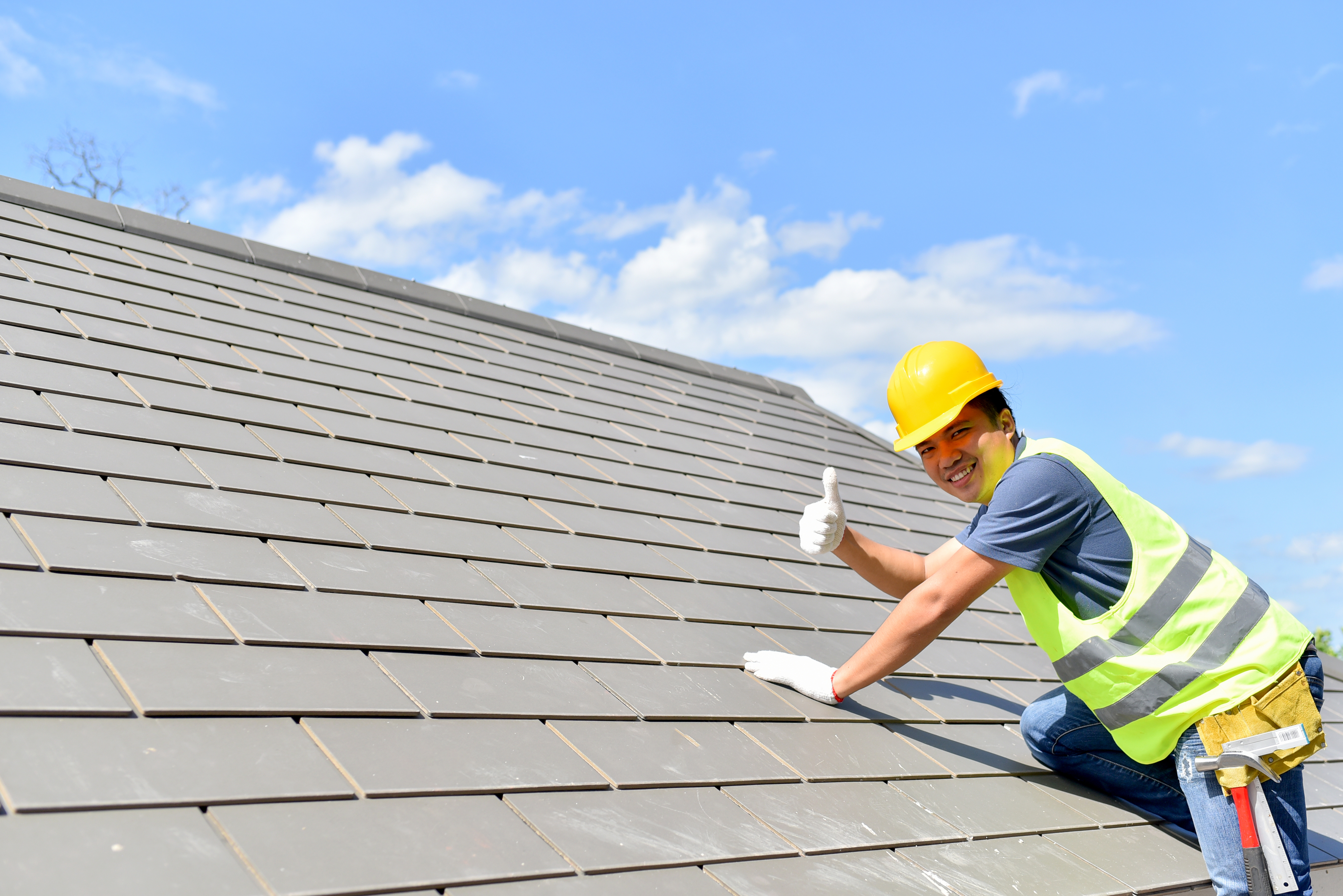 A contractor working on a roof gives a thumbs up to the camera